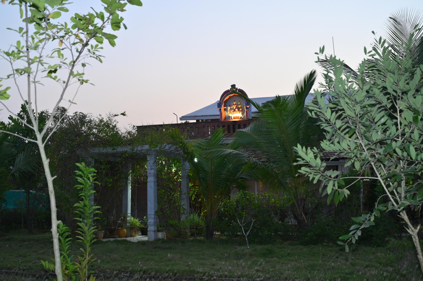 Mutram Heritage Stay at twilight — the rooftop shrine glowing across the paddy fields