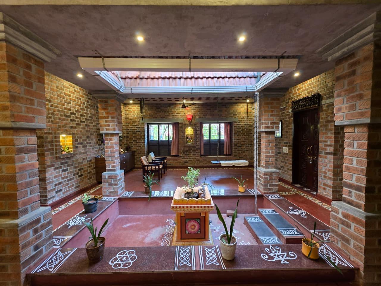 The central courtyard at Mutram — exposed brick walls, Athangudi tile floor, kolam patterns, skylight overhead