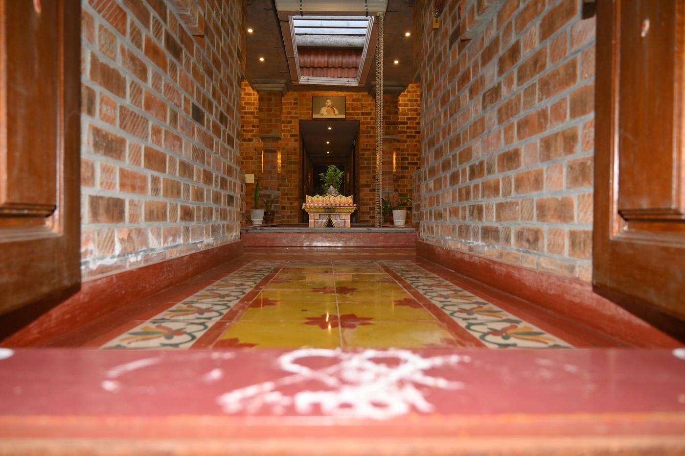 Pooja corridor at Mutram with Athangudi tile flooring, exposed brick walls, and traditional altar